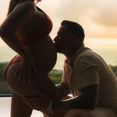 Luxury maternity photography at Kurá Boutique Hotel in Uvita. A tattooed partner kneels to kiss the expectant mother's bare belly during a beachside sunset session
