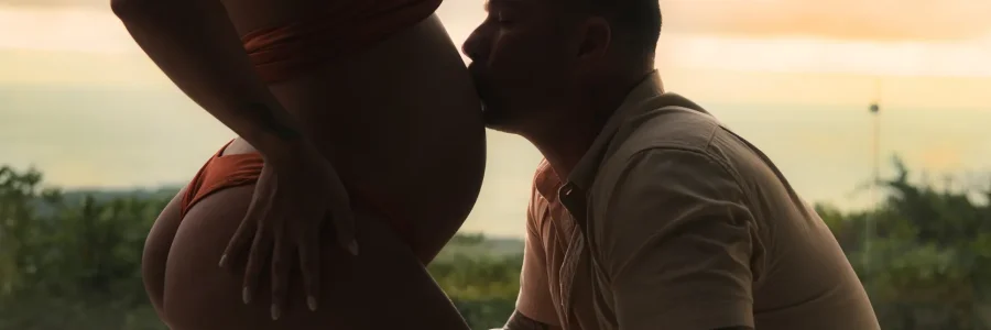 Luxury maternity photography at Kurá Boutique Hotel in Uvita. A tattooed partner kneels to kiss the expectant mother's bare belly during a beachside sunset session